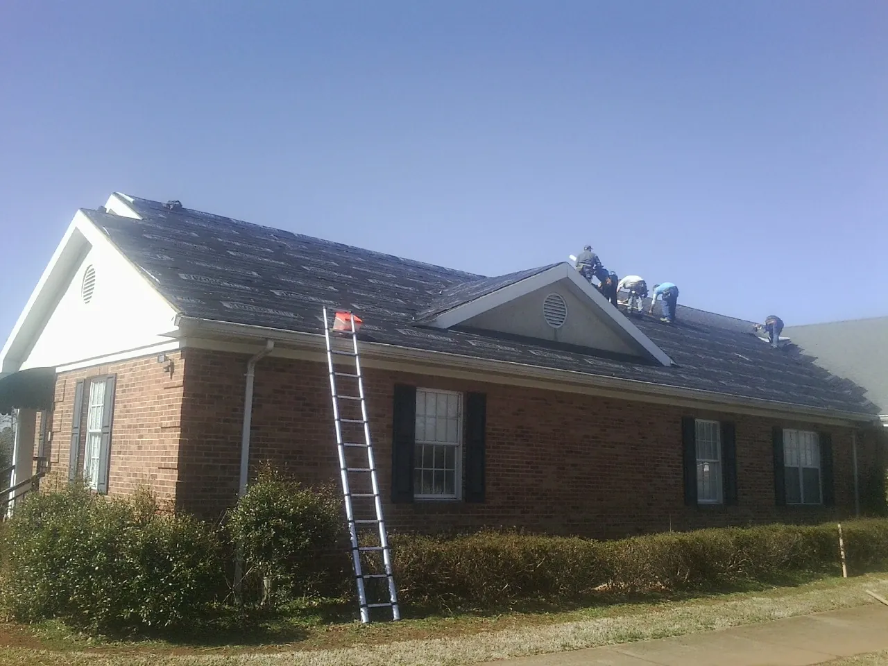 Crew tearing shingles off a brick ranch roof with a ladder set — Metal Roof Repair work by our crew in Acworth
