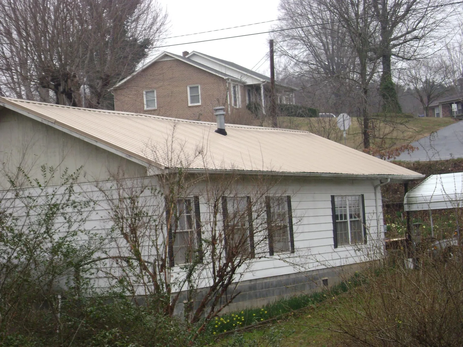 Tan metal roof on a white sided house set into a hillside — Commercial Roofing by Roofing Brothers in Acworth